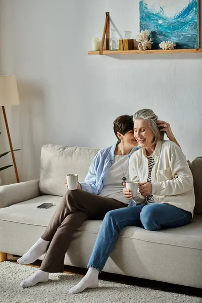 A loving mature lesbian couple sit together on a couch in a cozy living room. — Stock Photo