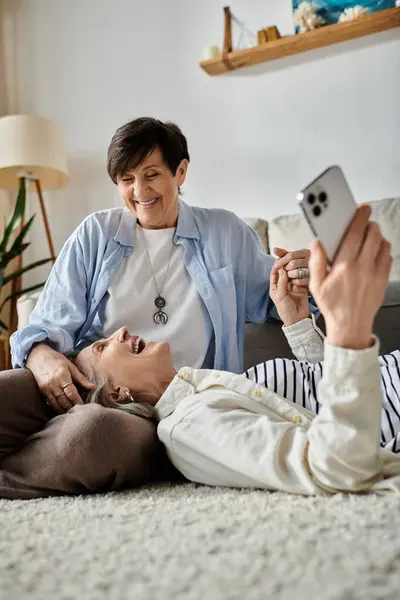 Two senior women laying on the floor, capturing a selfie moment of joy and friendship. — Stock Photo