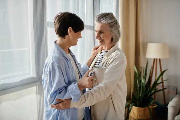 Two elderly women share a heartfelt hug by a sunlit window. — Stock Photo