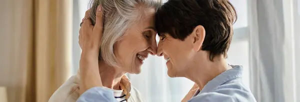 Two older women embrace lovingly in front of a window. — Stock Photo
