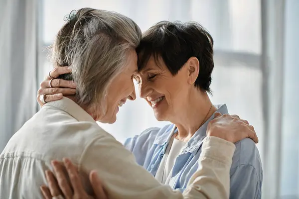 Two senior women hug warmly in front of a bright window. — Stock Photo