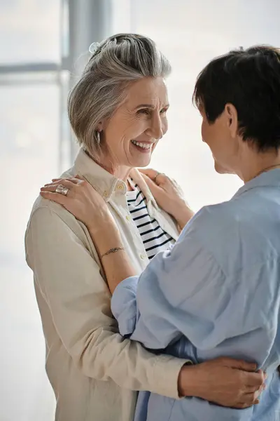 Two women, mature and loving, hugging by a window. — Stock Photo