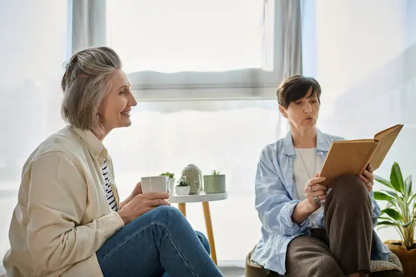 Two women, immersed in a book, sit together in a chair. — Stock Photo