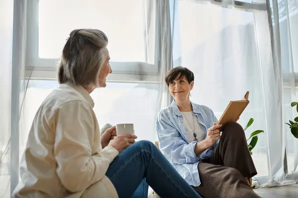 Due donne, una coppia lesbica matura amorevole, seduta sul pavimento davanti a una finestra. — Foto stock