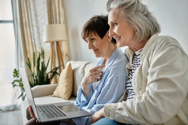 Two older women enjoy using a laptop while sitting on a couch together. — Stock Photo