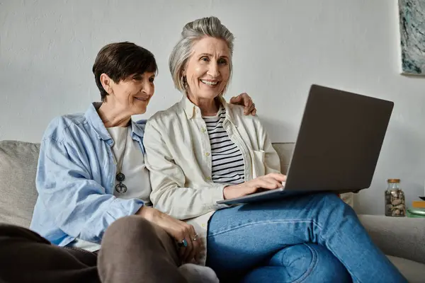 Two older women engrossed in laptop activities on a cozy couch. — Stock Photo