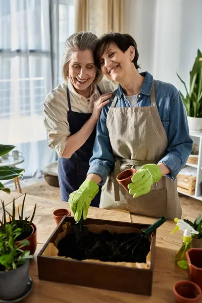 Two aproned women lovingly tend to the garden together. — Stock Photo