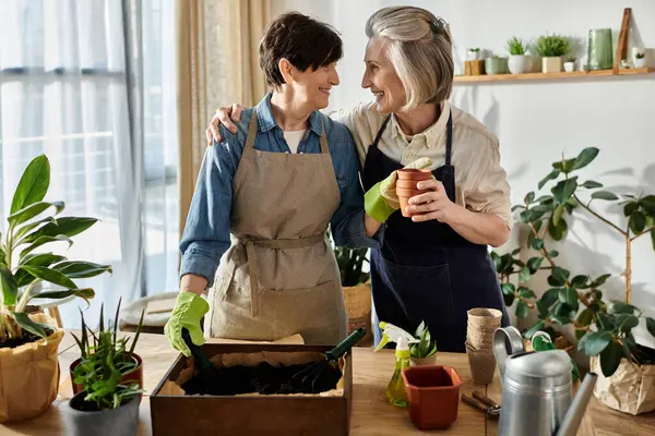 Two women in matching aprons tend to a lush potted plant. — Stock Photo
