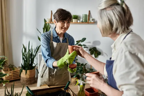 Two women in aprons help each other with plants in a garden. — Stock Photo