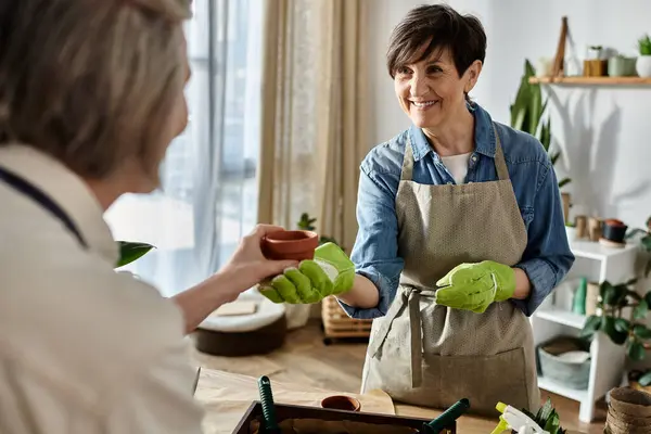 Una mujer le entrega una maceta de flores a otra mujer en un gesto tierno. - foto de stock