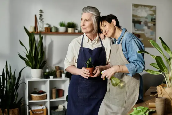 Two women in aprons caring for a potted plant. — Stock Photo