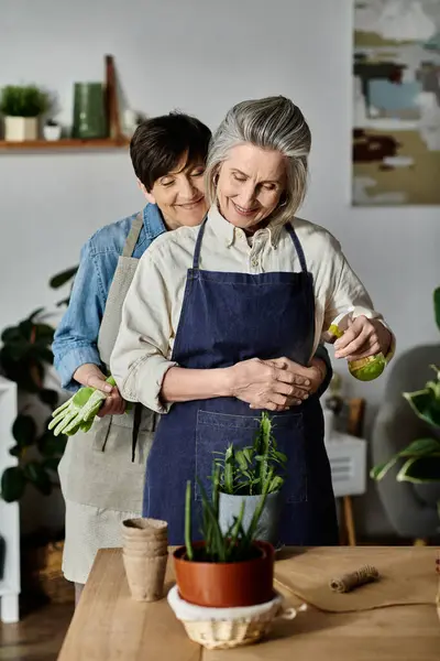Two women in aprons caring for a vibrant potted plant with love and care. — Stock Photo
