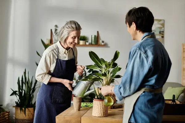 Mature couple, love-filled, watering plant in kitchen. — Stock Photo