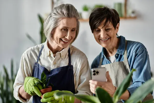 Two women in aprons engrossed in their phones. — Stock Photo