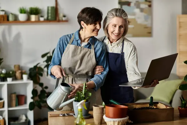 Two women in aprons engage with a laptop. — Stock Photo