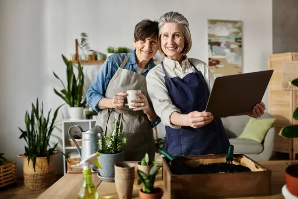 Two women standing gracefully in front of a potted plant. — Stock Photo