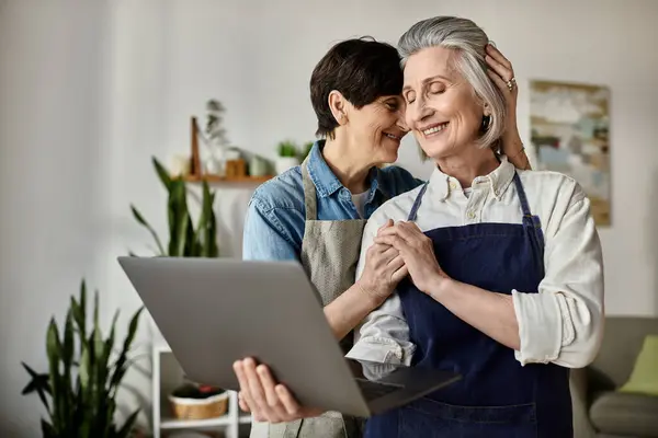 Two women, a loving mature lesbian couple, engrossed in a laptop screen together. — Stock Photo