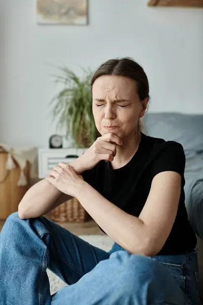 Middle-aged woman sitting on floor, hand on chin, deep in thought. — стокове фото