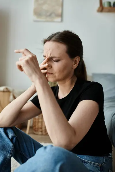 Middle-aged woman sitting, deep in thought, with finger on nose. — Stockfoto