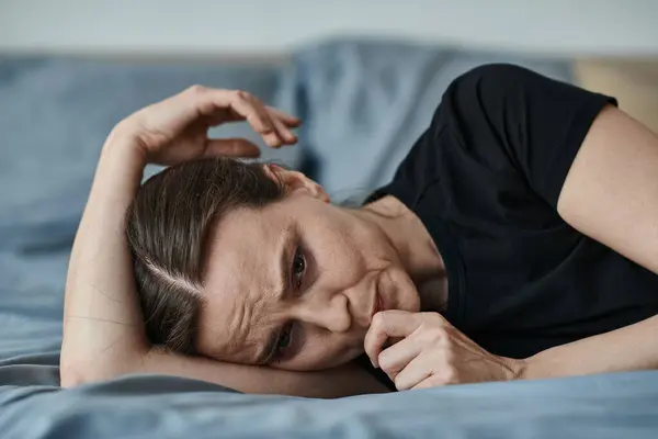 Middle-aged woman lays on bed, hand on head. — стоковое фото