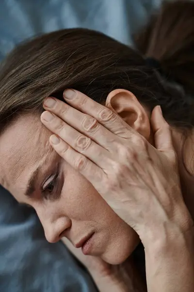 Middle-aged woman lies in bed, hands on head, deep in thought. - foto de stock