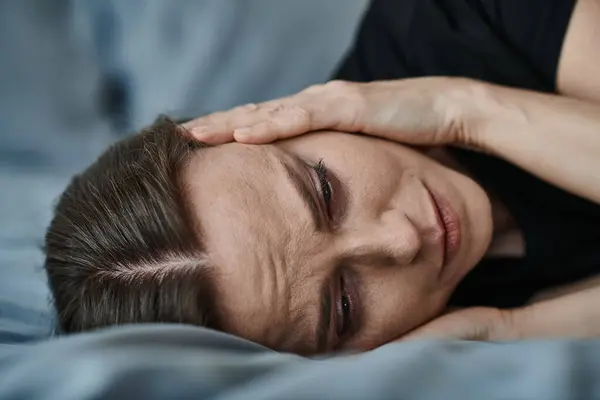 Middle-aged woman laying in bed with hand on head, deep in thought. — Stock Photo