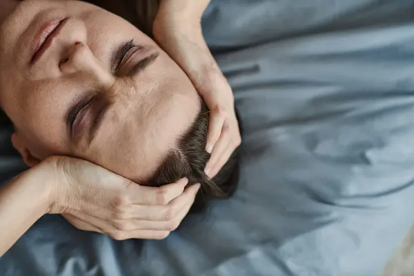 Middle-aged woman in bed, hands on head, deep in thought. - foto de stock