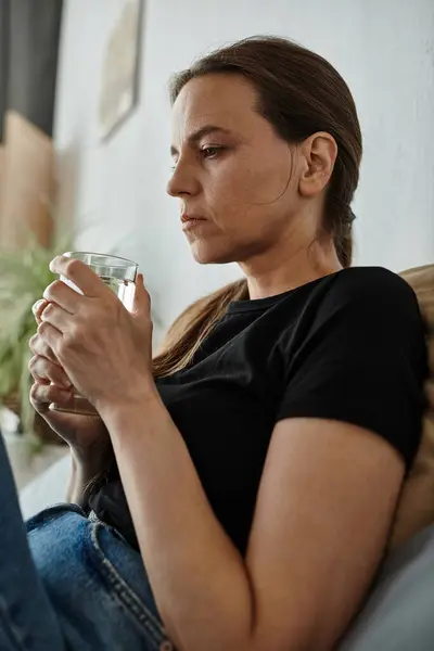Woman in contemplation on couch holding water. — Stock Photo