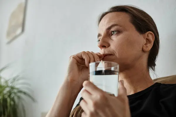 A woman finds solace on her couch, holding a glass of water. — Fotografia de Stock