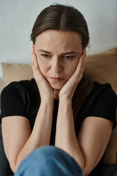 Middle-aged woman with hands on face sitting on couch at home. — Stock Photo