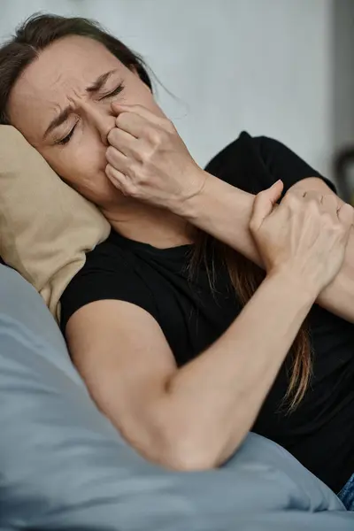 A middle-aged woman laying on a bed with her hand covering her face in a moment of reflection. - foto de stock