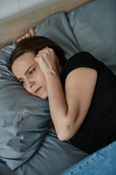 Middle-aged woman laying down, holding head in hand with contemplative expression. — Stock Photo