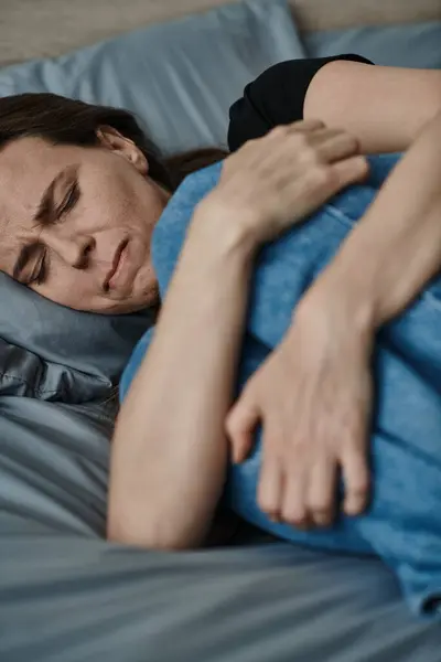 Middle-aged woman at home, laying in bed with hand on stomach. — Stock Photo