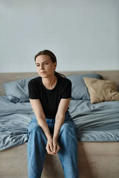 Middle-aged woman sitting on bed, looking downcast and forlorn. — Fotografia de Stock