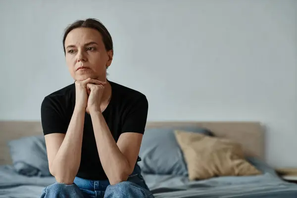 Middle-aged woman sitting on bed, deep in thought, hand on chin. — Stockfoto
