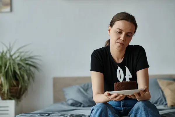 Middle-aged woman seated with chocolate cake on bed. — Stock Photo