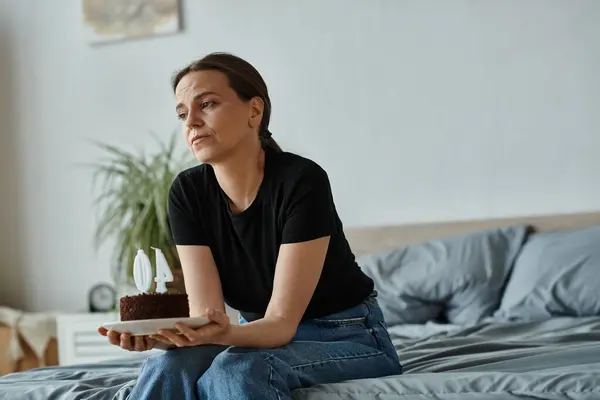 Middle-aged woman sitting on bed holding a cake. — стокове фото