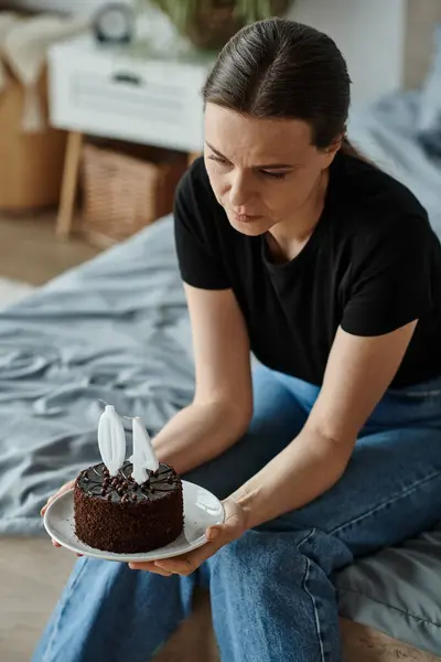 Woman holding a cake while sitting on her bed. — Stock Photo