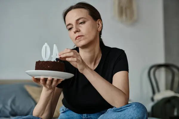 Middle-aged woman sitting on floor in contemplation with cake in front. — Stockfoto