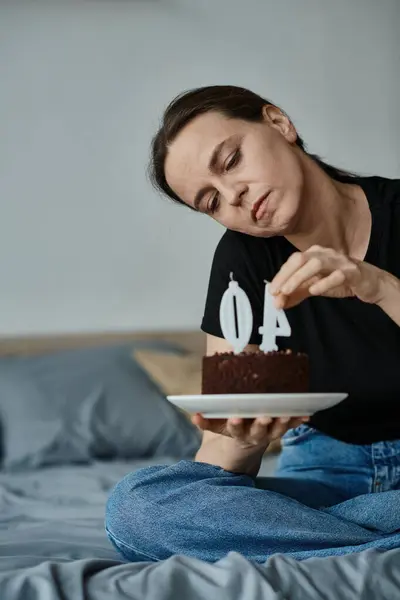 Middle-aged woman thrilled holding special 40th birthday cake on her bed. — Stockfoto