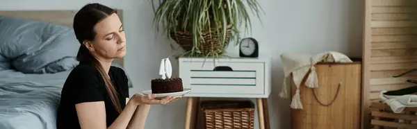 Middle-aged woman holds cake while standing in front of bed. — Stock Photo