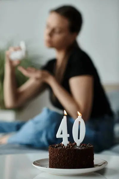 Woman sitting beside a 40th birthday cake on a bed. - foto de stock