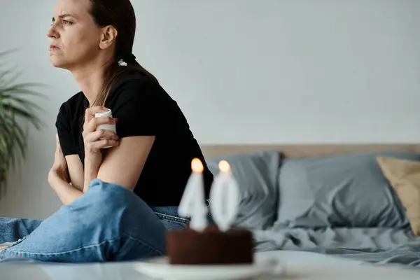 A middle-aged woman sits on a bed, holding a candle in her hands in a moment of reflection. — стоковое фото