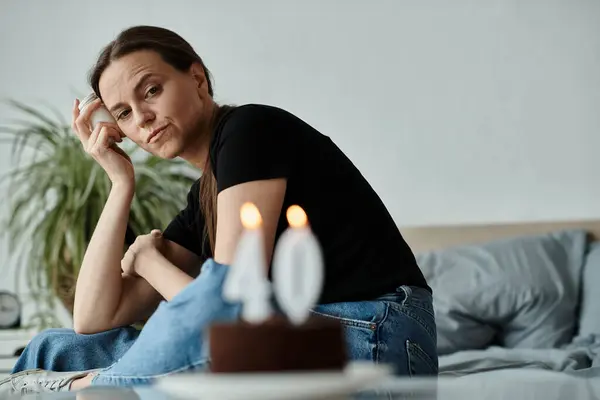 Middle-aged woman in deep thought sits with birthday cake in front of her. — Stock Photo