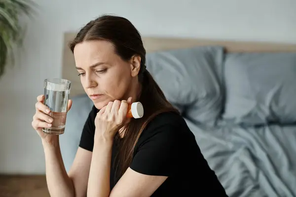 A middle-aged woman peacefully holds a glass of water on her bed. — Stock Photo