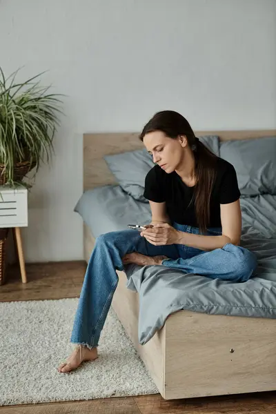 Middle-aged woman, emotionally distressed, sits on bed, engrossed in phone. — Stock Photo