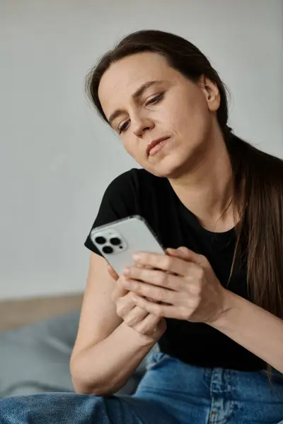 Middle-aged woman sitting on bed, absorbed in phone screen. — Stockfoto