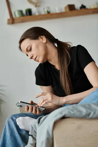 Middle-aged woman on couch, absorbed in phone screen. — Stockfoto