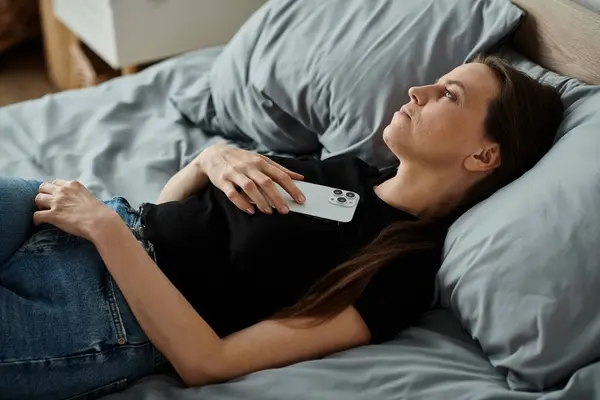 A woman in bed with her phone, engaging deeply with digital connection. — Stockfoto