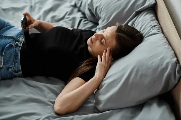 A woman in bed, holding her phone. — Stock Photo